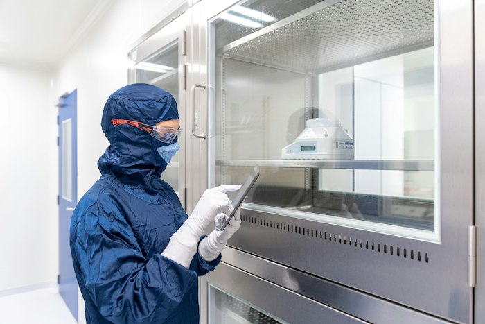 A cleanroom operator in protective gown checking data on a tablet beside the equipment